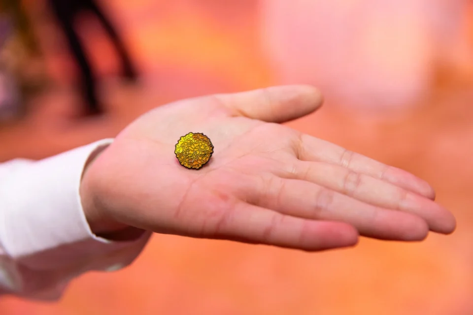 A person holding a small marigold pin in their hand.